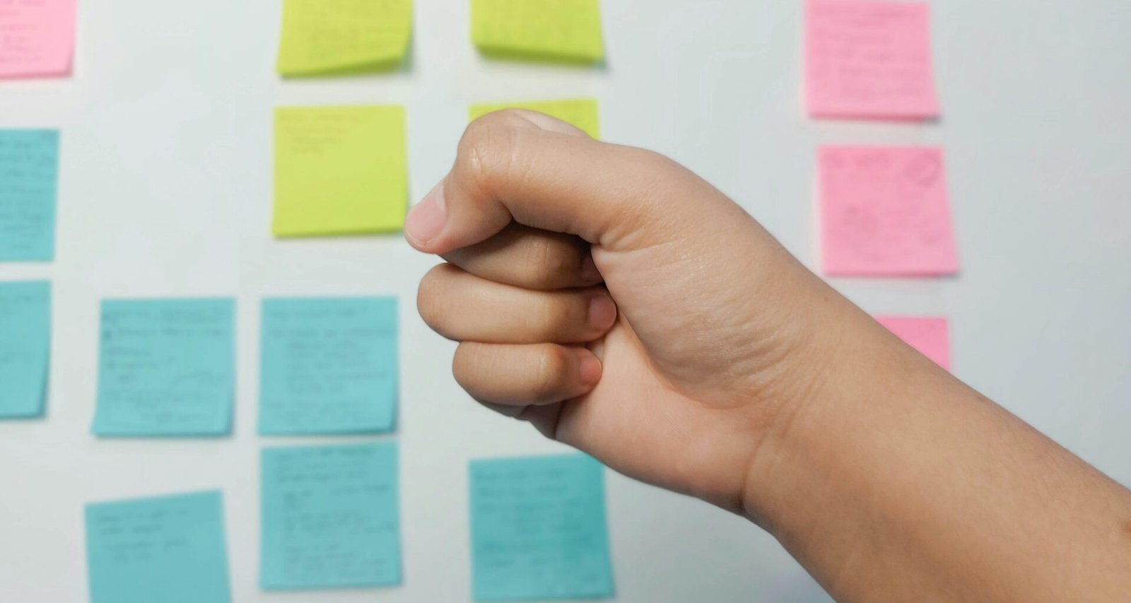 Eine Person hält gelbe und pinke Haftnotizen in der Hand, um Aufgaben im Team zu koordinieren und Ideen festzuhalten.