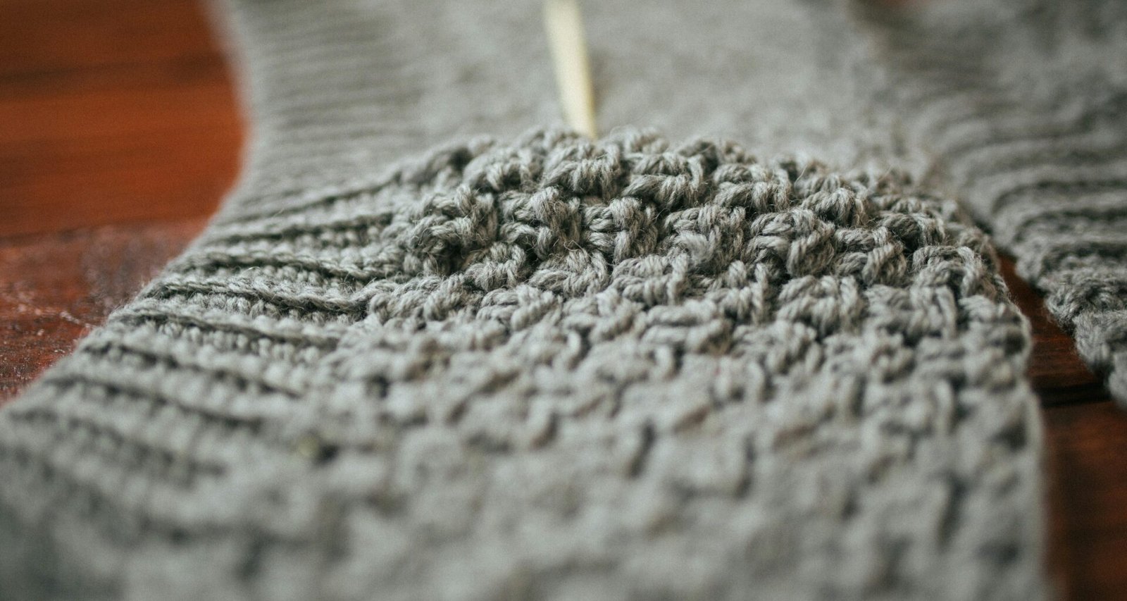 Eine Person hält ein graues Stricktextil und präsentiert die Struktur des Stoffes gut sichtbar.