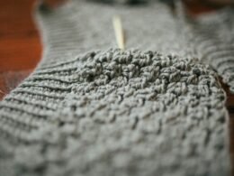 Eine Person hält ein graues Stricktextil und präsentiert die Struktur des Stoffes gut sichtbar.