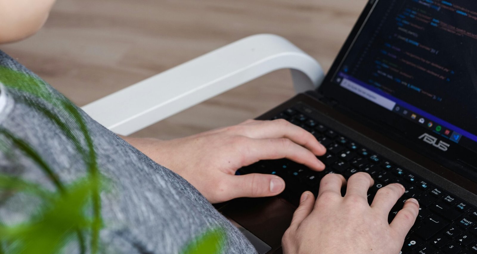 Person arbeitet an einem schwarzen Asus Laptop an einem Tisch – Symbol für moderne Technologie im Berufsalltag.