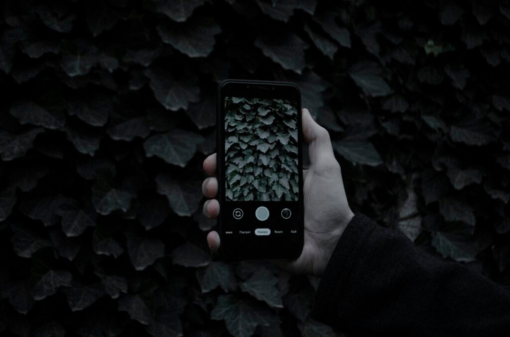 Eine Person hält ein schwarzes iPhone 5 in der Hand, Fokus auf das Smartphone und dessen Rückseite.