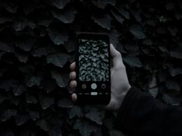 Eine Person hält ein schwarzes iPhone 5 in der rechten Hand vor neutralem Hintergrund.