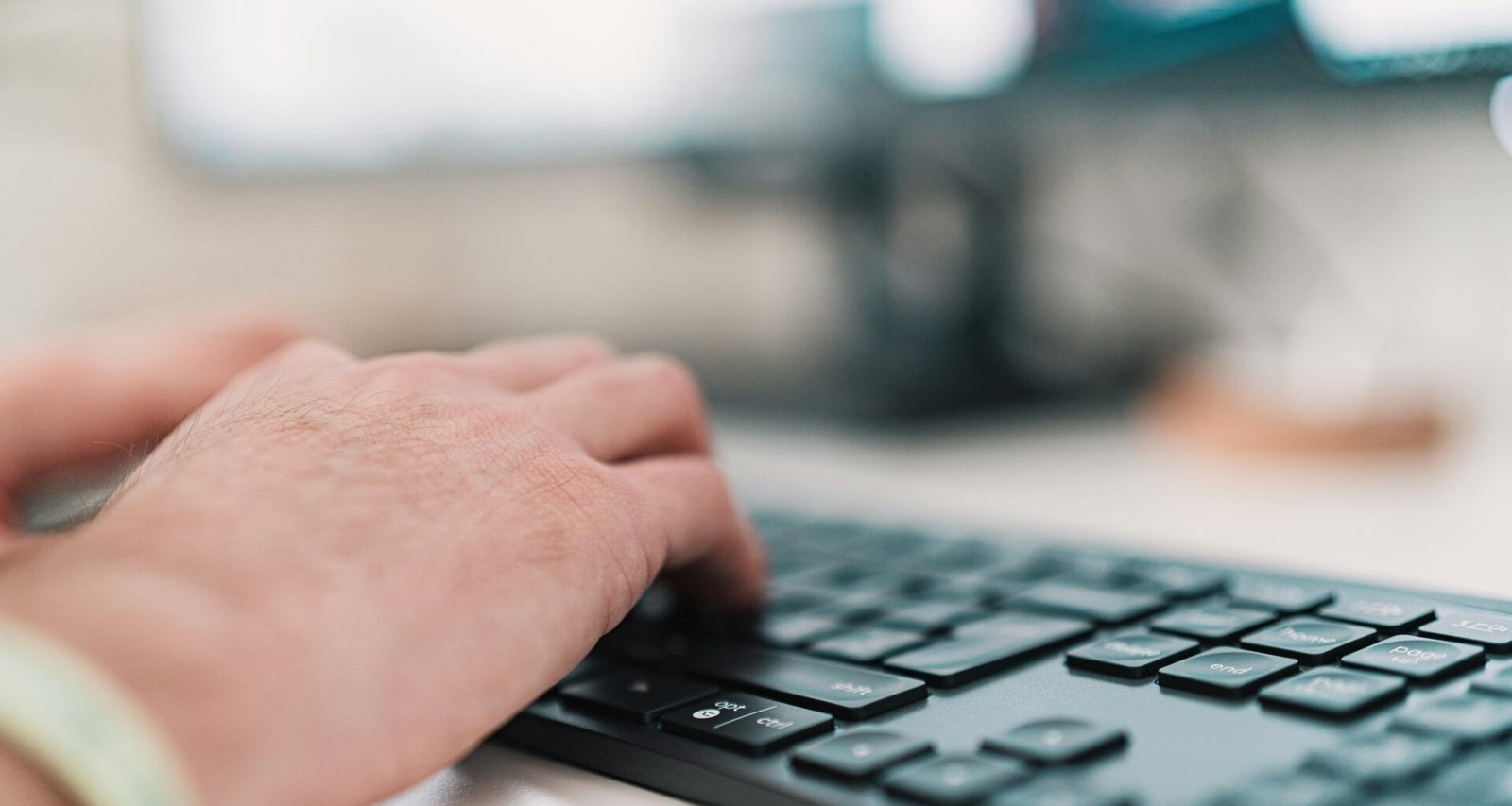 Person tippt auf einer schwarzen Computertastatur während der Arbeit im Büro am Schreibtisch