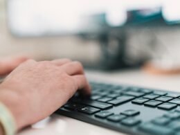 Person tippt auf einer schwarzen Computertastatur während der Arbeit im Büro am Schreibtisch