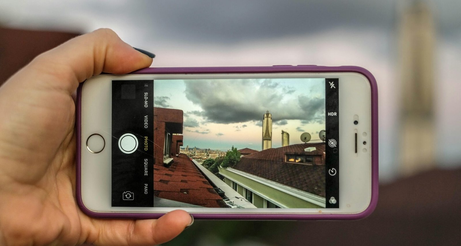 Person hält ein silbernes iPhone 6 mit violetter Schutzhülle in der Hand, Fokus liegt auf dem Smartphone