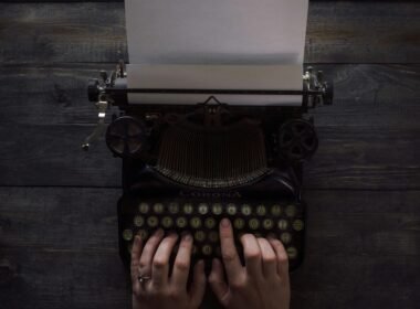 Eine Person hält eine weiße und schwarze Schreibmaschine in den Händen, Symbol für Kreativität in der digitalen Arbeitswelt.