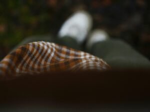 Person in kariertem Oberteil und grüner Hose mit weißen Schuhen steht auf Gehweg, trendiger Streetstyle-Look.