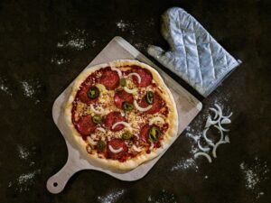 Frisch gebackene Pizza, serviert auf einem braunen Holztablett, von oben fotografiert auf hellem Untergrund