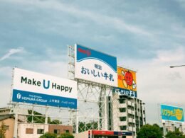 Mehrere große Leuchtreklamen mit japanischer Schrift sind in einer urbanen Umgebung deutlich sichtbar.