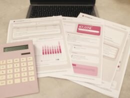 Auf einem Tisch liegen Rechnungen, ein Taschenrechner und ein Laptop, umgeben von Stiften – Symbol für digitale Finanzorganisation.