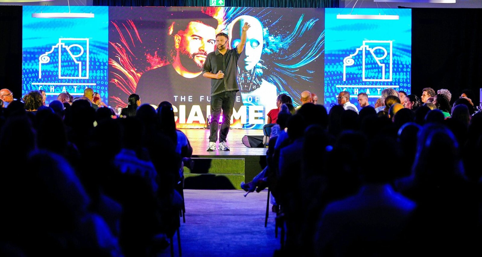 Ein Redner präsentiert auf einer Bühne vor einer sitzenden Zuhörerschaft während einer Konferenz.