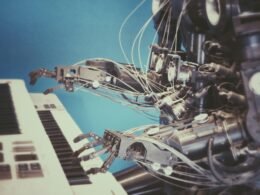 Ein silberner Roboter sitzt an einem klassischen Klavier und spielt auf den Tasten. Hintergrund ist neutral gehalten.