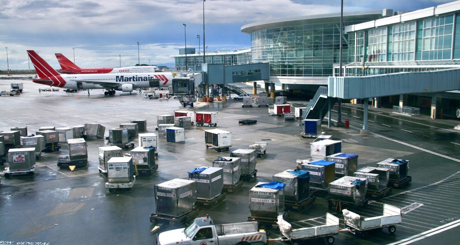 Rollfeld eines Flughafens mit mehreren Gepäckwagen und einem Flugzeug während der Abfertigung