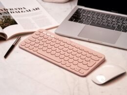Pinke Tastatur, Maus und ein Laptop stehen ordentlich auf einem Schreibtisch in einem modernen Home-Office-Umfeld