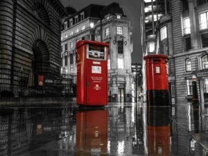 Rote Londoner Briefkästen stehen nachts auf nasser Straße, beleuchtet von Straßenlaternen und umgeben von Stadtverkehr.