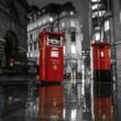Zwei rote Postkästen in London auf einer regennassen Straße bei Nacht mit Lichtern im Hintergrund