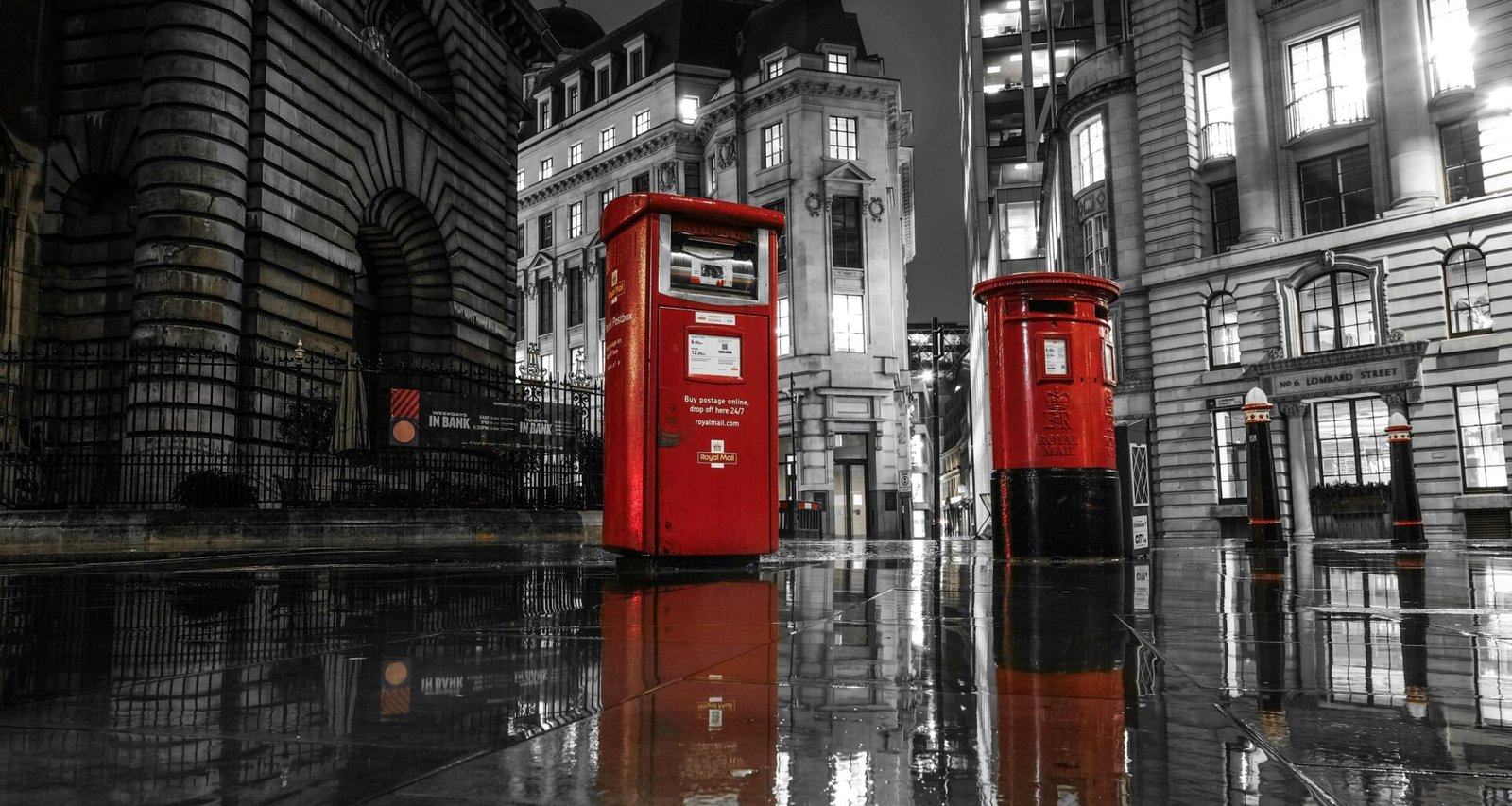 Zwei rote Postkästen in London auf einer regennassen Straße bei Nacht mit Lichtern im Hintergrund