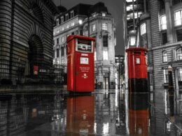 Zwei rote Postkästen in London auf einer regennassen Straße bei Nacht mit Lichtern im Hintergrund