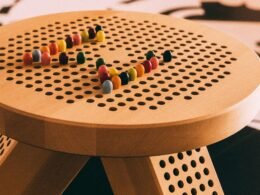 Rote und gelbe Perlen liegen auf einem braunen, runden Holztisch in einer hellen Umgebung.