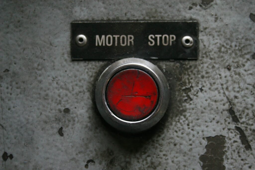 Roter Not-Aus-Knopf auf silberner Metallplatte, Fokus auf industrielle Sicherheit und Steuerungselemente