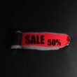 Rotes Preisschild mit dem Aufdruck ‚Sale 50%‘ auf schwarzem Untergrund, geeignet für E-Commerce und Online-Marketing-Artikel.