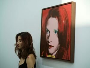 Rothaarige Frau malt an einer Leinwand, eine weitere Frau steht daneben in einem hellen Atelier.