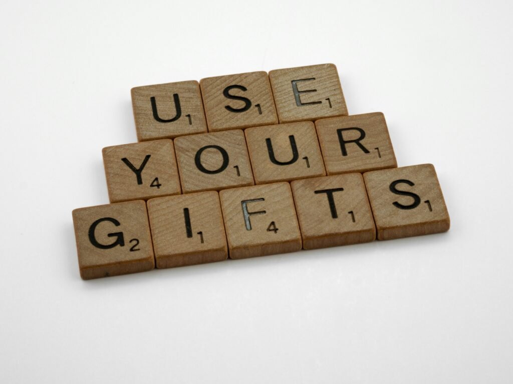 Scrabble-Holzbuchstaben bilden den Schriftzug 'use your gifts' auf einer hellen Oberfläche, fotografiert aus der Vogelperspektive.