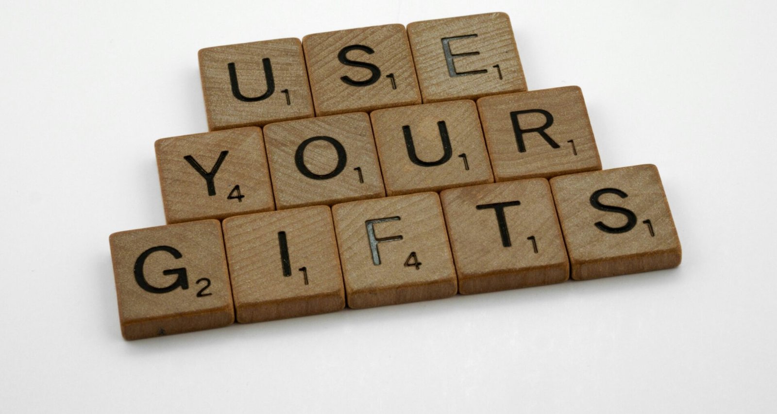 Scrabble-Holzbuchstaben bilden den Schriftzug 'use your gifts' auf einer hellen Oberfläche, fotografiert aus der Vogelperspektive.
