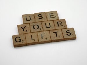 Scrabble-Holzbuchstaben bilden den Schriftzug 'use your gifts' auf einer hellen Oberfläche, fotografiert aus der Vogelperspektive.