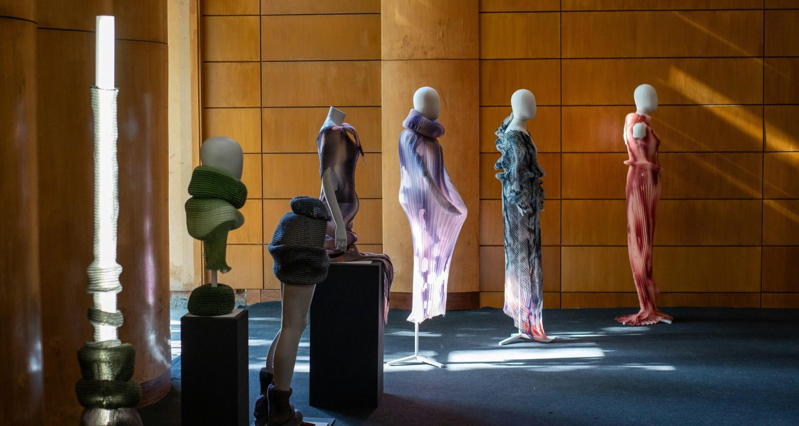 Mehrere Schaufensterpuppen mit abstrakten Skulpturen und ausgefallener Kleidung stehen in einem hellen Ausstellungsraum.