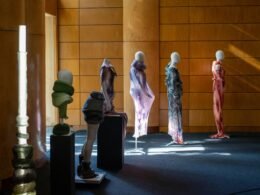 Mehrere Schaufensterpuppen mit abstrakten Skulpturen und ausgefallener Kleidung stehen in einem hellen Ausstellungsraum.