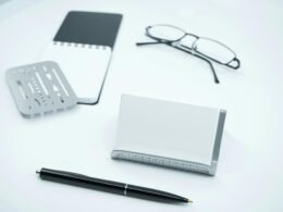 Schwarze Brille liegt neben weißem Druckerpapier und einem schwarzen Stift auf einem Schreibtisch, ideale Büroausstattung.