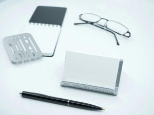 Schwarze Brille liegt neben weißem Druckerpapier und einem schwarzen Stift auf einem Schreibtisch, ideale Büroausstattung.