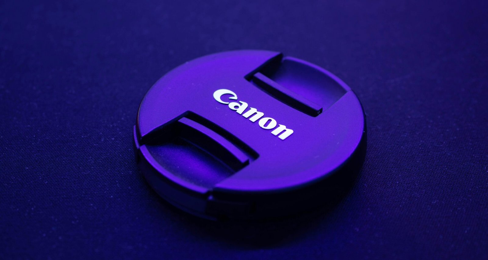 Ein schwarzer Canon Kamera Objektivdeckel liegt auf einem weißen Untergrund, fotografiert aus der Nähe.