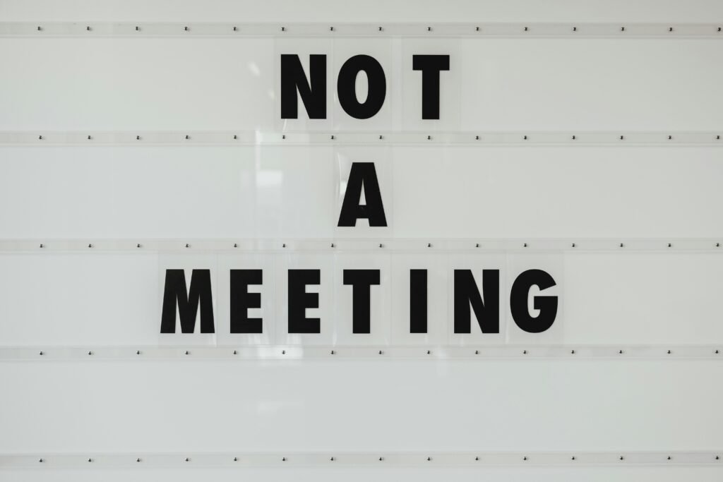 Schwarzes Hinweisschild mit Aufschrift „Note a meeting“ an grauer Wand im modernen Bürogebäude
