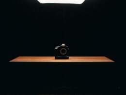 Schwarze Kompaktkamera auf einem braunen Holztisch, aufgenommen im Nahbereich, zeigt das klassische Kameradesign.