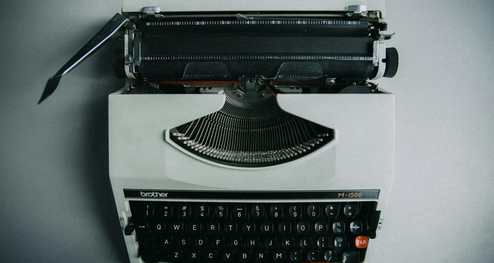 Eine schwarze Schreibmaschine mit Tastatur und Papierrolle auf einem Tisch, aufgenommen aus seitlicher Perspektive