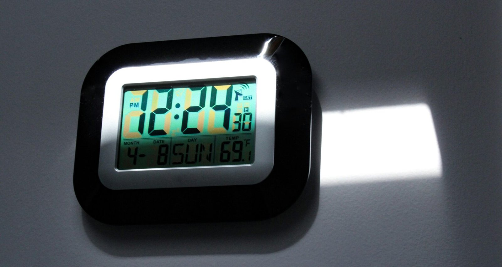 Schwarze und graue digitale Wanduhr mit gut lesbarem LED-Display auf einer neutralen Wand