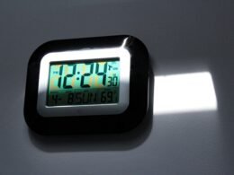 Schwarze und graue digitale Wanduhr mit gut lesbarem LED-Display auf einer neutralen Wand