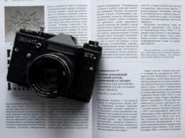 Schwarze und silberne Nikon DSLR Kamera liegt auf weißem Druckerpapier, Fokus auf Technik und Design.