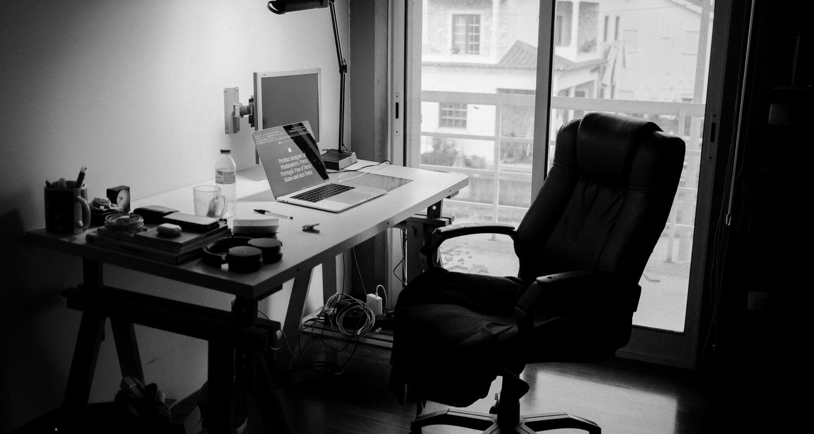 Ein schwarzer Büro-Drehstuhl steht neben einem weißen Holzschreibtisch in einem modern eingerichteten Arbeitszimmer.