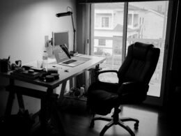 Ein schwarzer Büro-Drehstuhl steht neben einem weißen Holzschreibtisch in einem modern eingerichteten Arbeitszimmer.