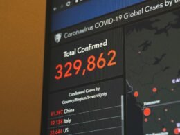 Schwarzer Flachbildfernseher mit sichtbar eingeschaltetem Bildschirm, nah aufgenommen, vor neutralem Hintergrund