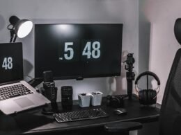 Ein schwarzer Flachbildschirm-Computer steht auf einem schwarzen Holztisch in einer modernen Büroumgebung.