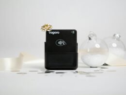 Schwarzes Kartenlesegerät mit goldener Schleife und weihnachtlichen Ornamenten auf einem Tisch