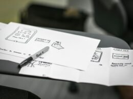 Ein schwarzer Marker liegt diagonal auf einem Stapel weißer Druckerpapiere und symbolisiert die Vorbereitung für Notizen oder Skizzen.