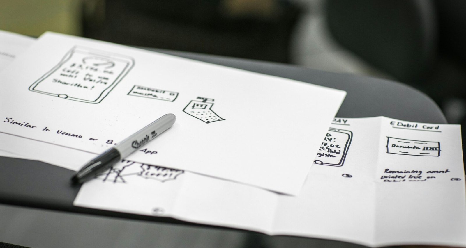 Schwarzer Marker liegt auf mehreren weißen Druckerpapieren, fotografiert aus der Vogelperspektive