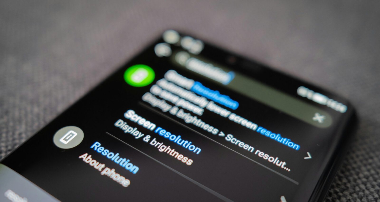 Schwarzes Android-Smartphone auf einem strukturierten grauen Textilstoff, flach aus der Vogelperspektive fotografiert