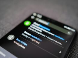 Schwarzes Android-Smartphone auf einem strukturierten grauen Textilstoff, flach aus der Vogelperspektive fotografiert