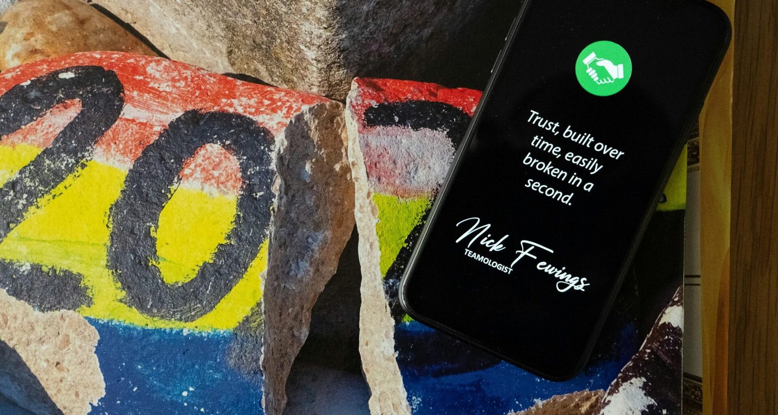 Schwarzes iPhone 5 auf blau-gelb-rot gemustertem Felsen, fotografiert von oben, geeignet für Tech- und Marketingartikel